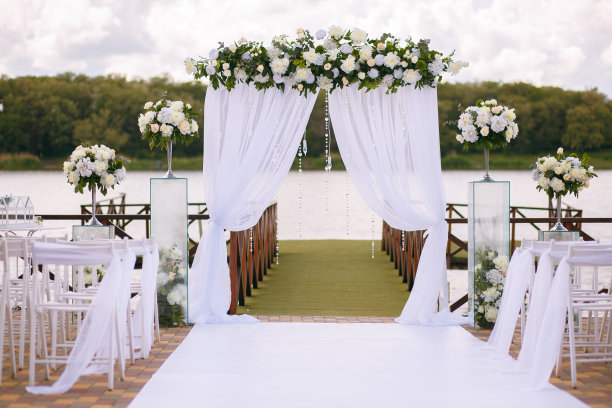 由树枝、鲜花和绿叶组成的婚礼拱门坐落在河边的绿草地上图片下载