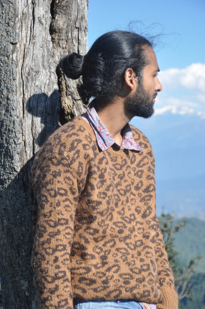 一个长得很帅的年轻人，头发挽成圆髻，在大自然中靠树站着，看着别处图片下载