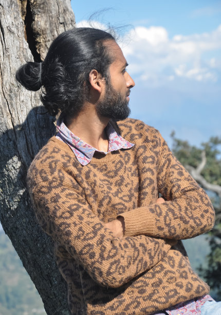 一个挽着发髻的年轻男子倚靠在树上，双臂交叉，眼睛向一边看图片下载