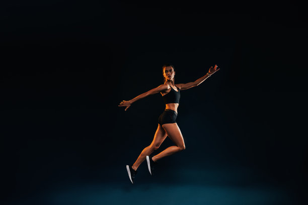 苗条的女人在黑色背景下工作。女运动员在演播室里跳。图片下载