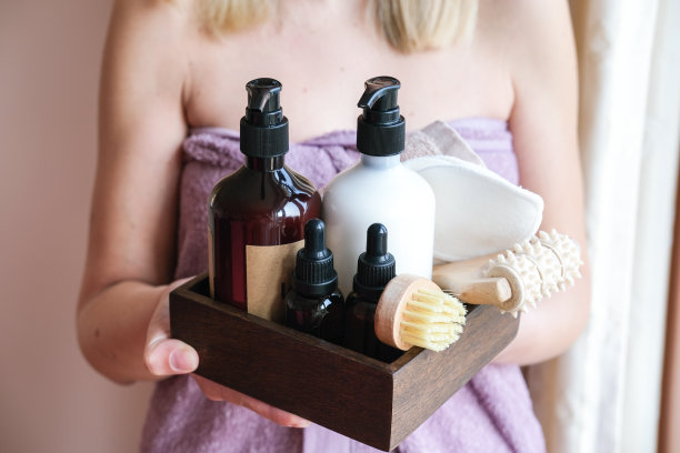 身体和面部护理美容沐浴套装。乳液，精油，面霜，按摩刷和瘦身霜，放在一个篮子里，在一个年轻的女人手中。图片下载