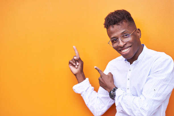 非裔美国商人穿着漂亮的衬衫，戴着橙色背景的眼镜，微笑着看着相机，双手和手指指向一边图片下载