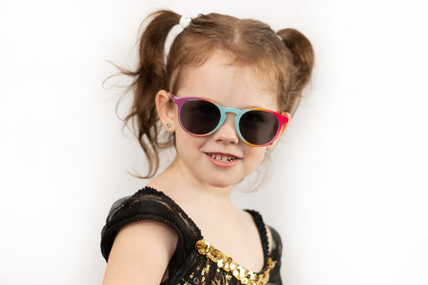 一个扎着两个马尾辫，穿着黑色和金色连衣裙的爱笑的顽皮女孩。白色背景下的戴墨镜儿童影棚照片图片下载
