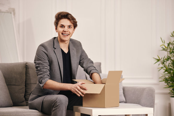 坐在沙发上打开纸板箱的男人。图片下载