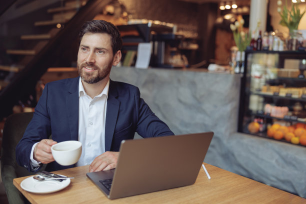 在豪华咖啡馆里，白种帅哥带着笔记本电脑坐在桌前。经营理念。图片下载