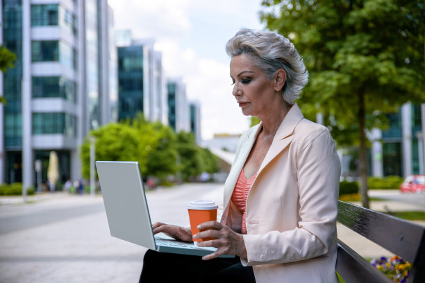 年老有吸引力的女人使用笔记本电脑前的商业大厦图片下载