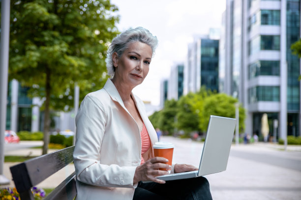 年老有吸引力的女人使用笔记本电脑前的商业大厦图片下载