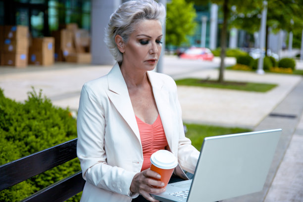 年老有吸引力的女人使用笔记本电脑前的商业大厦图片下载