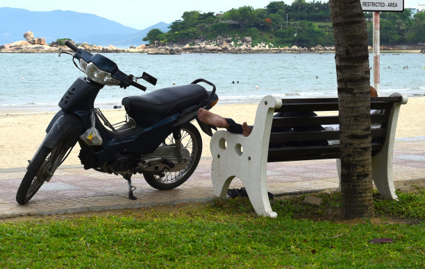 越南芽庄，一名越南男子睡在摩托车旁的长凳上图片下载