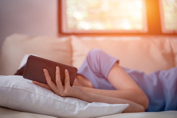 躺在沙发上的女人正在使用智能手机。放松的假期。图片下载