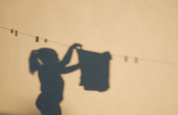 一个模糊的女性形象的照片。女人把洗好的衣服挂在晾衣绳上。图片下载