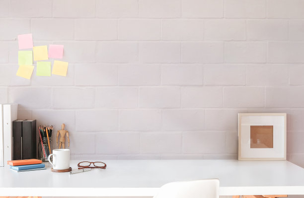 创意的工作场所，空的相框，咖啡杯和白色桌子上的用品，彩色的便签贴在砖墙上。图片下载