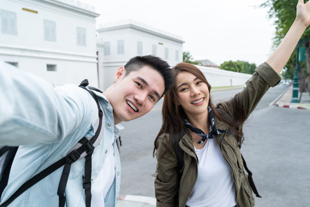 亚洲背包客夫妇用手机自拍，在城市里拍照。迷人的男女游客在街上旅游，用智能手机录制视频在泰国度假旅行。图片下载
