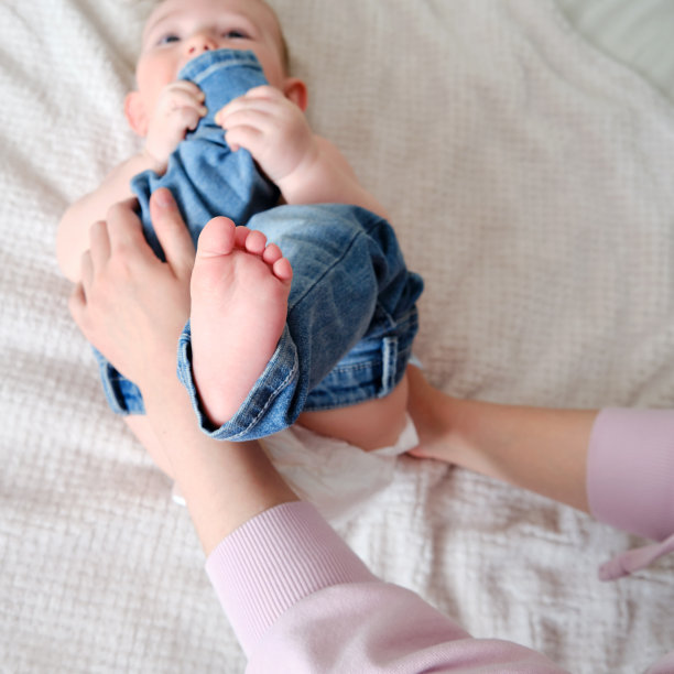 一位母亲给一个小男孩穿上牛仔裤。妈妈给孩子穿上床上的衣服。图片下载