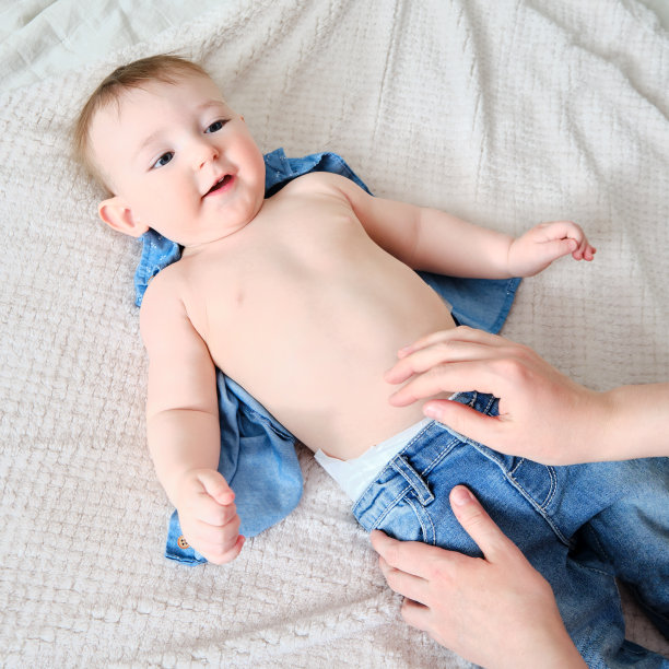 一位母亲给一个小男孩穿上牛仔裤。妈妈给一个快乐的孩子穿上床上的衣服。图片下载