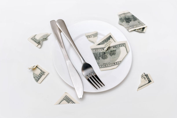 白色盘子上餐叉和餐刀旁的撕裂百元美钞图片下载