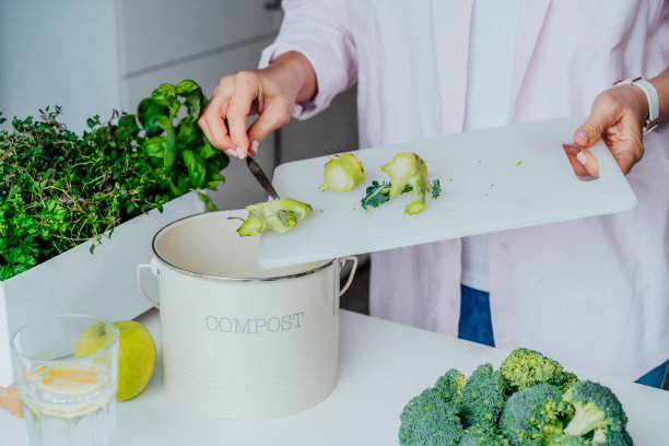 将厨房垃圾堆肥，回收利用。近距离妇女刮，扔蔬菜切剩菜到垃圾，堆肥垃圾箱，而在她的厨房做饭。环保、生态图片下载