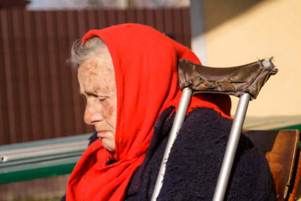 迷离的乌克兰老妇人披着红色披肩，拄着拐杖坐在外面。女人85岁。孤独的人。特写镜头的脸。模糊。悲伤的人。痴呆、记忆。副本的空间。的焦点图片下载