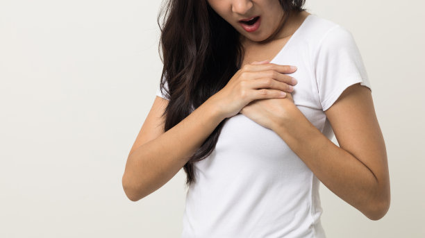 亚洲女性，25岁左右。她感到胸口一阵疼痛，握住她的手，紧紧地捏着。她心脏病发作，需要治疗。穿着白衬衫站在孤立的背景上。图片下载