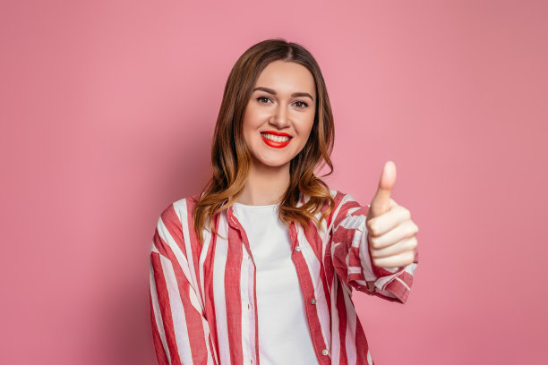 年轻女子在条纹衬衫显示像手势孤立在工作室的粉红色背景。学习外语图片下载