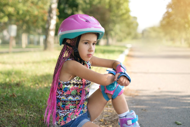 一个戴着运动防护头盔、戴着护膝的严肃周到的孩子坐在那里，望着复印空间。暑假娱乐和户外运动活动图片下载
