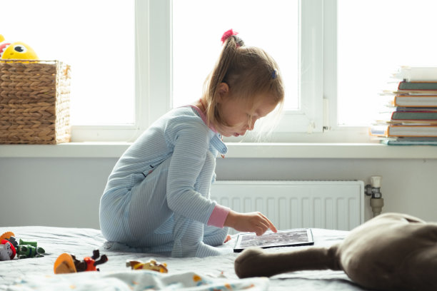 小女孩床上用平板看动画片玩游戏。图片下载