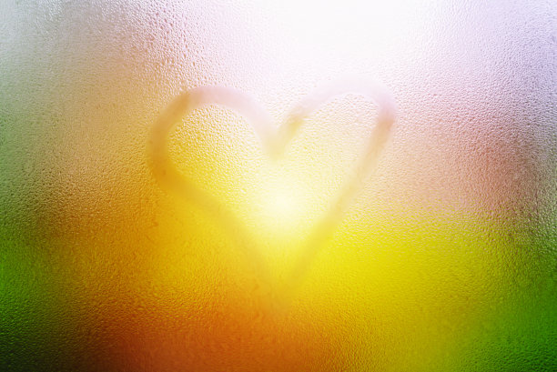 一颗心画在露珠晶莹的玻璃窗上，被雨滴和阳光模糊着。有选择性的重点。图片下载