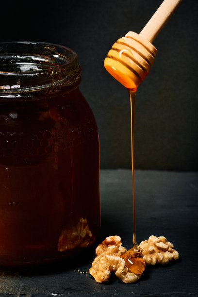 一罐有机蜂蜜，用勺子把蜂蜜倒在核桃上图片下载