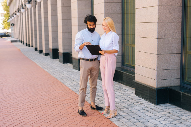 在办公楼旁边的城市街道上，欢快的男同事和女同事正在剪贴板上讨论文件。图片下载