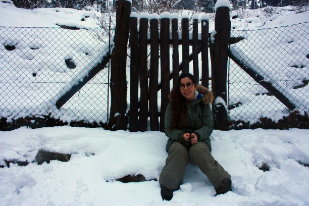 在意大利托斯卡纳，一个女孩穿着冬装坐在白天雪中的木栅栏前图片下载