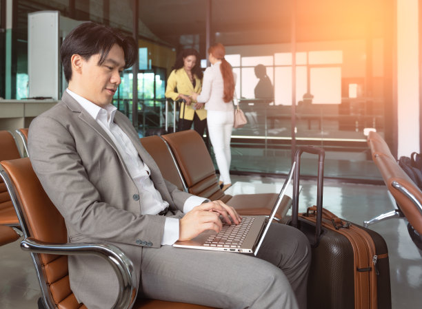 在机场大厅等待旅行时，商人在行李旁边用笔记本电脑工作图片下载