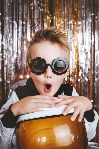 滑稽的孩子的肖像在宇航员的幻想服装有乐趣的节日背景与箔窗帘装饰。孩子的生日派对，万圣节，新年，庆祝任何节日。图片下载