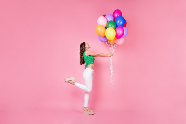 正面开朗的女孩的全长侧面照片持有气球享受周年聚会穿好看的衣服孤立在柔和的颜色背景图片下载