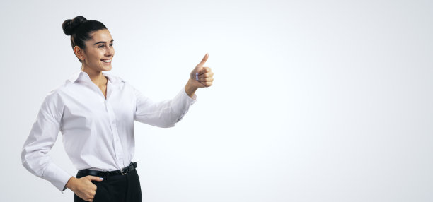 点赞概念，快乐的女孩穿着白衬衫，在浅灰色墙壁背景上竖起大拇指，有空白的地方供您撰写文字，样机图片下载