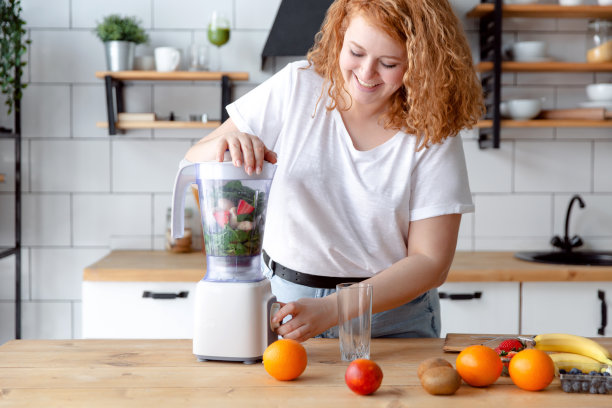 一个美丽微笑的女人在家庭厨房准备奶昔的肖像。图片下载