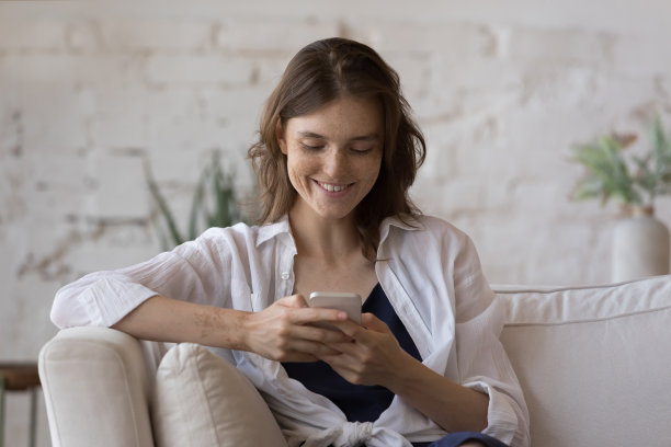 快乐的雀斑智能手机用户女孩坐在家里的沙发上图片下载
