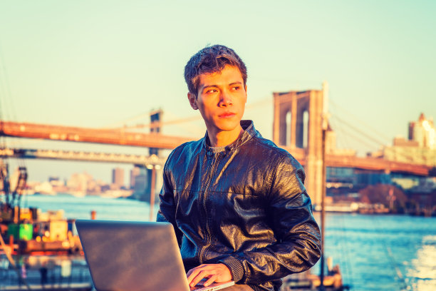 年轻的亚裔美国大学生在纽约市河边的户外用笔记本电脑工作图片下载