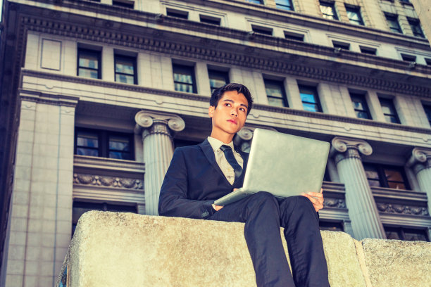 年轻的亚裔美国大学生在纽约市办公大楼外用笔记本电脑工作图片下载
