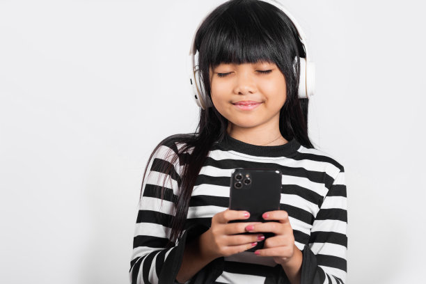亚洲小孩10岁了，喜欢用手机听音乐，戴着无线耳机图片下载