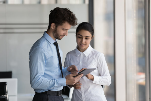 两个忙碌的年轻同事穿着正装在使用平板电脑图片下载