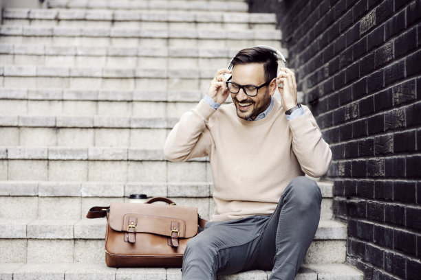 一个快乐的男人坐在街上的楼梯上，戴着耳机。图片下载