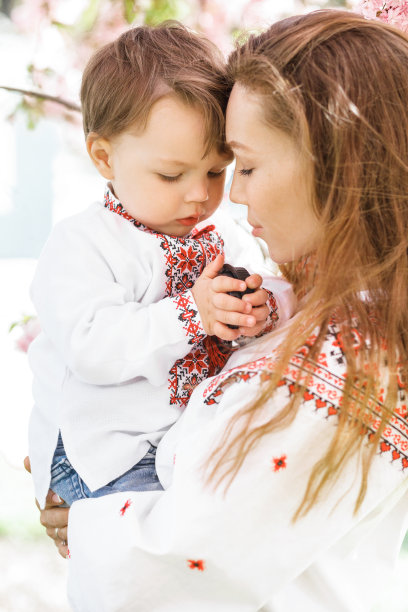 小男孩被妈妈抱在怀里。在春暖花开的花园里，女人和孩子在外面玩耍。两个人的家庭肖像。春天风景背景。图片下载