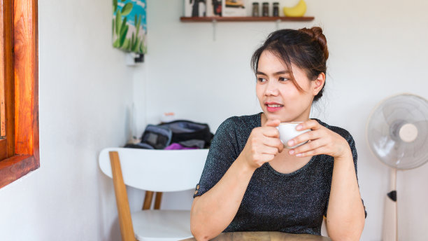 肖像美丽的亚洲女人坐在一张桌子与一杯咖啡放松微笑在她的房间在家里度假。白色的泰国女孩图片下载