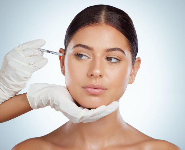 漂亮女人在做面部填充或注射肉毒杆菌。年轻的白人模式孤立在灰色的工作室背景与copyspace。皮肤科医生注射病人在抗衰老美容程序图片下载