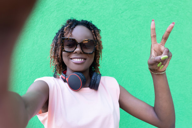 一名戴着太阳镜微笑着的非洲裔美国女性在绿色背景下自拍。积极的情绪图片下载