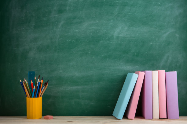 教育与阅读理念——教室里的木桌上摆放着一组组五颜六色的书籍，背景是黑板图片下载