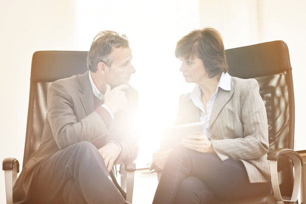 两个同事在现代办公室里使用平板电脑。一名成熟的商人和一名女商人在网上用触摸屏工作，谈论商业事务图片下载