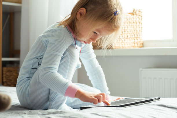 小女孩床上用平板看动画片玩游戏。图片下载