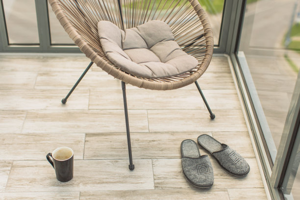 阳台上有靠垫的柳条椅。窗外的景色很美。出租的房子。上午休息。休闲的概念。阳光明媚的一天。地板上有一杯茶。舒适的拖鞋图片下载