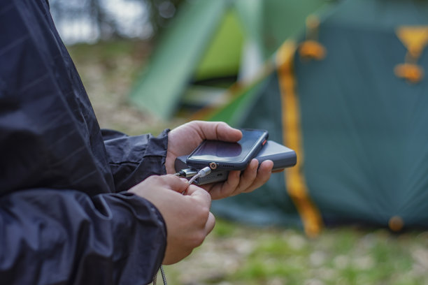男人手持智能手机，用充电宝在旅游帐篷背景下充电。便携式旅行充电器。图片下载